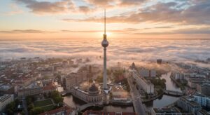 A sweeping aerial view of the TV Tower (Fernsehturm) piercing through a layer of morning mist overlo
